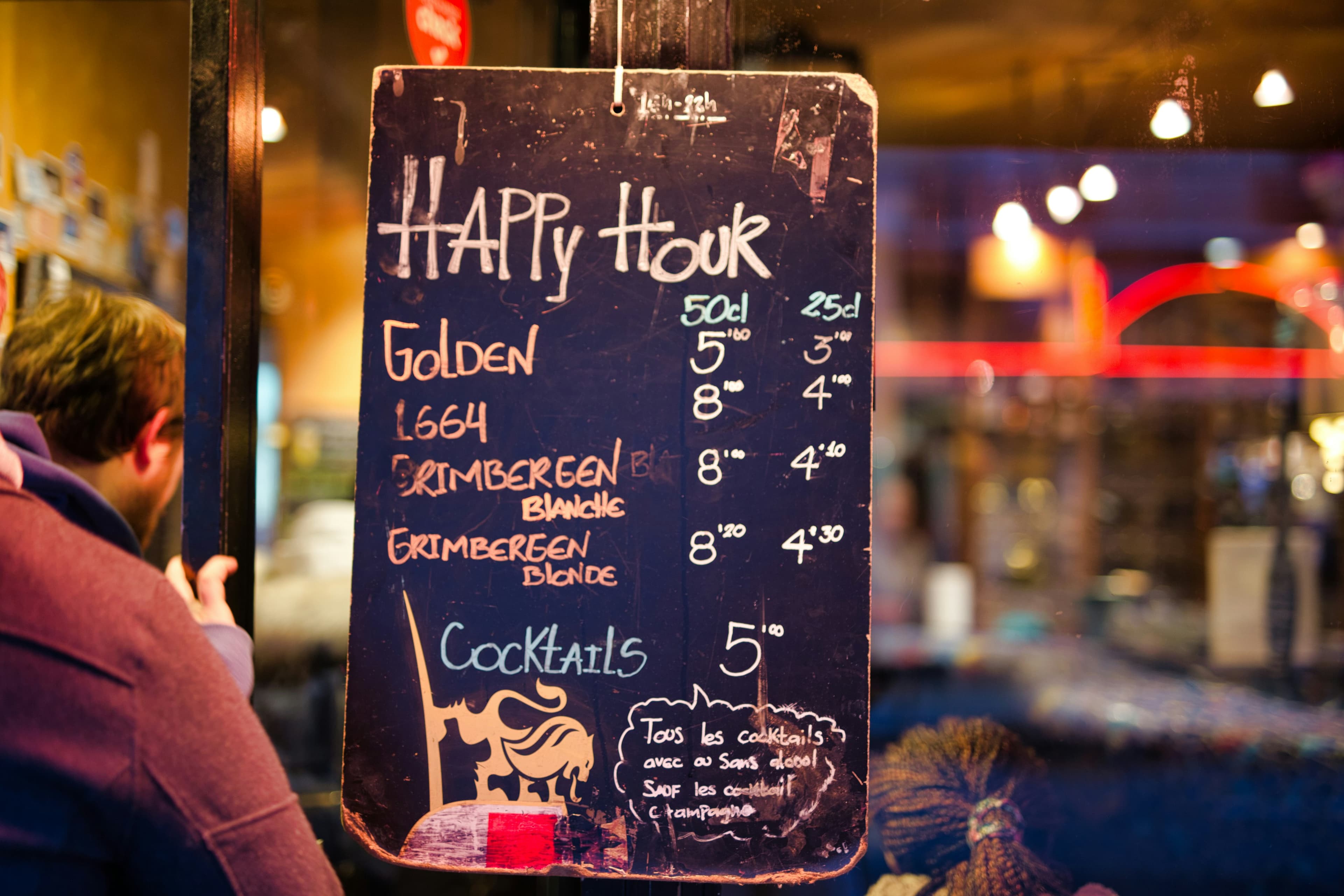 A person pausing to read a handwritten happy hour sign outside a local restaurant